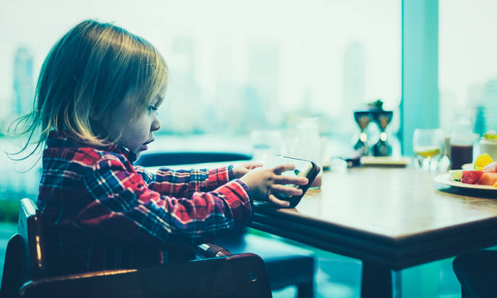 A toddler is using a smartphone at the breakfast table